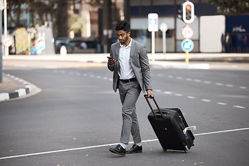 Image showing Phone, travel and luggage with a business man walking in the city for an international trip. Mobile, communication and suitcase with a young male employee typing a text message on a street commute