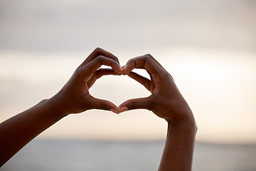 Image showing Hand, heart and love sign at the beach with romantic, emoji and happiness hands gesture. Outdoor, sea and ocean with person holding romance, loving and valentines sign on holiday in nature at sunset