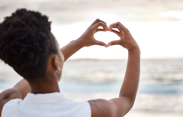 Image showing Woman hand, heart and love sign at the beach with romantic, emoji and happiness hands gesture. Outdoor, sea and ocean with female person back with kindness sign on holiday in nature at sunset