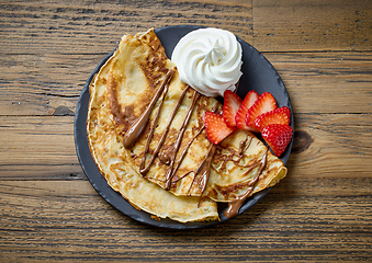 Image showing freshly baked crepes with whipped cream and strawberries