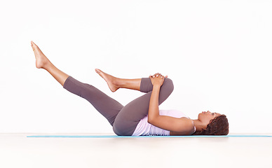 Image showing Yoga, leg stretch and black woman in studio on a fitness and workout mat for training. Isolated, white background and African female person lying on the ground with sport stretching for wellness