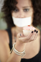 Image showing Cupcake in hand, eating disorder and a woman on diet and tape over mouth to stop or lose weight. Face, covering and restriction of female suffering with anorexia, body dysmorphia or bulimia problem