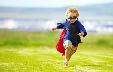 Image showing Young boy, costume and running in park, playing and carefree outdoor with happiness or playful child on grass. Freedom, energy or youth and happy kid in cape or goggles fun on green lawn with mockup