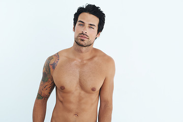 Image showing Portrait, body and muscle with a sexy man in studio on a white background for masculine desire. Shirtless, tattoo and manly with a handsome young male model posing topless for rugged sensuality