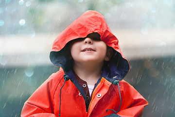 Image showing Happy boy, red raincoat and little child playing or having fun with the raindrops and outdoors. Smile, kid and looking up at the sky or enjoying rainfall and showers on bokeh background