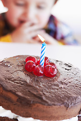 Image showing Birthday cake closeup, young kid and celebration candle with dessert at home with a child. Chocolate, cherry and candles to celebrate a boy at a party with sweets on a kitchen table in a house