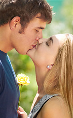 Image showing Love, kiss and happy with couple in nature for romantic, bonding and affectionate. Happiness, flowers and gift with man and woman kissing in garden park on date for spring, care and valentines day