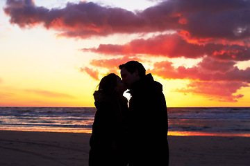 Image showing Beach, sunset and couple silhouette kiss in nature with love, freedom and romance outdoors. Shadow, romantic and people kissing at sunrise, sweet and together for travel, vacation or holiday in Bali