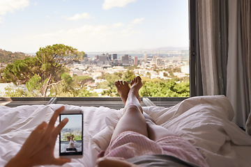 Image showing Bed, phone and window view with feet, relax and photography for blog, review and screen in hotel. Woman, hand and smartphone for profile picture with cityscape, nature or social media app in bedroom