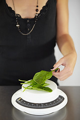 Image showing Hand, scale and spinach in kitchen for diet, food or eating disorder with leaves for meal plan. Woman, mental health and vegetable leaf to lose weight with anorexia, bulimia or starving in home