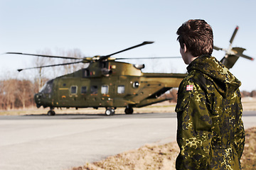 Image showing Army, military or soldier man with a helicopter outdoor for transportation, Denmark war and pilot mission. Male person for combat, flight or air force service in camouflage uniform to watch or patrol