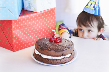 Image showing Birthday cake, kid and curious of food at party with gifts and dessert at home with a hungry child. Chocolate, sneaky and snack to celebrate a boy at a party feeling temptation for sweets in house