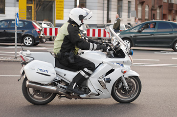 Image showing Police, motorbike and road safety officer working for protection and peace in an urban neighborhood in Denmark. Security, law and legal professional or policeman on a motorcycle ready for service