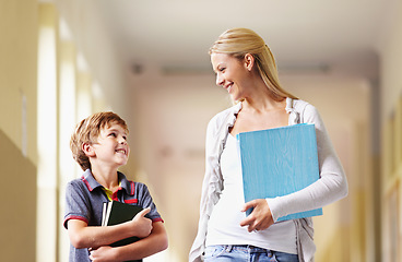 Image showing Talking, teacher and boy walking, hallway and happiness with advice, help and education. Male child, student and woman with a smile, lobby and conversation with joy, communication and development