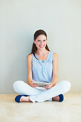 Image showing Portrait, tablet and a woman sitting legs crossed on the floor of her home browsing social media with a smile. Happy, technology and app with a young female person using the internet against a wall