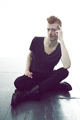 Image showing Portrait, ginger and man sitting on a floor with hand on head or wearing black or in thought for fashion and against white wall. Mohawk, dark and young guy thinking in punk clothes or rock and roll