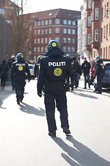 Image showing Security, justice and back of policeman in the city working to patrol protest or march. Law enforcement, public service and safety guard or officer in uniform for protection in town street in Denmark