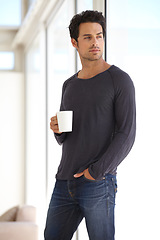 Image showing Handsome, young and man with a cup of coffee standing by the window in a vacation house. Calm, relax and attractive male person drinking a capuccino in the living room while thinking or daydreaming.