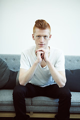 Image showing Serious, couch and portrait of man with ginger hair or sit in a lounge in thought or for hipster fashion and against white wall. Sofa, think and young person with funky, casual style or relax at home