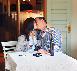 Image showing Love, kiss and a couple on a wine farm together in celebration of love or their anniversary. Kissing, romance or dating with a loving man and woman at a table in a winery feeling happy while bonding