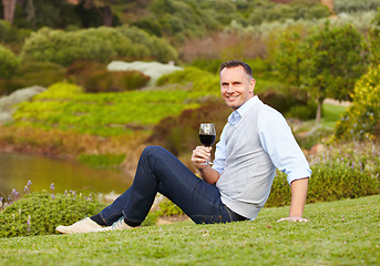Image showing Mature man with red wine outdoor, relax with smile in nature with alcohol drink, leisure and travel to countryside. Happy male person with alcoholic beverage in glass, satisfied and relaxing in park