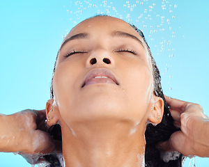 Image showing Face, hair and shower by woman in studio for cleaning, wash and shampoo on blue background. Girl, haircare and model relax in water splash, hygiene and grooming, skincare and wellness isolated