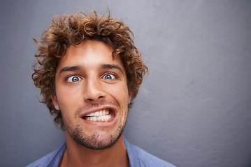 Image showing Young man, portrait and silly face for funny or goofy expression against a gray wall background. Male with crazy humor or impression looking and posing in playful happiness or fun manner and attitude