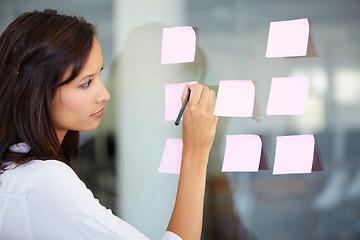 Image showing Business woman, writing and planning for brainstorming, strategy or ideas on glass board at the office. Female employee working on tasks for reminder, sticky note or project plan at the workplace