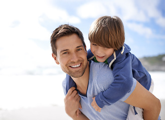 Image showing Father, child or family at beach for portrait, travel or holiday in summer with a smile for piggy back fun. A man and kid or son playing together on vacation at sea with a blue sky and happiness