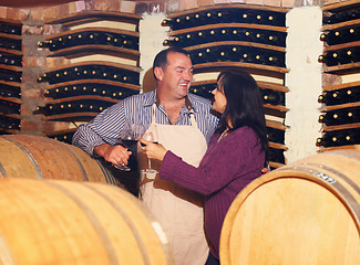 Image showing Wine, oak barrels and a couple in a cellar for the storage, production or fermentation of alcohol at a winery. Love, manufacturing or industry with a mature man and woman drinking a beverage together