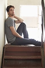 Image showing Portrait, depression and lonely with a man on a staircase in his home, sitting on the landing by a window. Alone, mental health and relax with a handsome young male on steps or stairs in his house