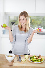 Image showing Choice, sweets and woman decide on healthy food in a kitchen for a diet and holding an apple and candy in home. Portrait, smile an happy female person with fruit for nutrition as lunch meal