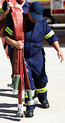 Image showing Firefighter, team and carrying hoses for emergency, rescue or fire drill from truck outdoors. Firefighters working together in practice lifting big liquid pressure pipes outside station or department