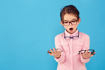 Image showing Surprise, mockup and child with glasses choice for vision or eye care promotion isolated in a blue studio background. Wow, decision and young girl shocked by sale, discount and deal for eyewear