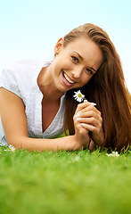 Image showing Portrait, happy and woman with daisy on grass, lying down on field and enjoying spring on vacation outdoor. Smile, flower plant and beauty of female person relaxing, mockup and having fun in nature.