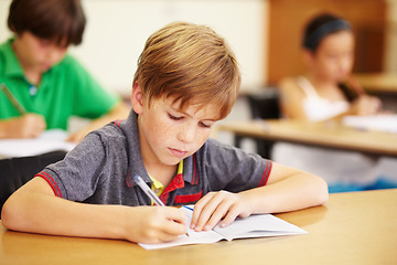 Image showing Boy kid, school classroom and writing test with focus, concentration and thinking for education goals. Male child, book and pen in class for assessment, studying or learning at desk for scholarship