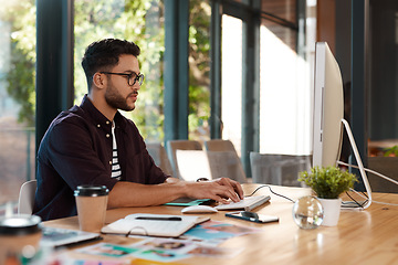 Image showing Designer, man and typing online on computer while working at desk for research or creative work. Male entrepreneur person with glasses and focus for reading or writing email with internet connection