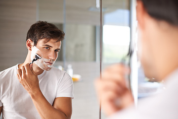 Image showing Mirror, shaving and face of man in bathroom for facial grooming, wellness and skincare at home. Health, skincare and serious male person shave beard for hygiene, cleaning and hair removal with razor