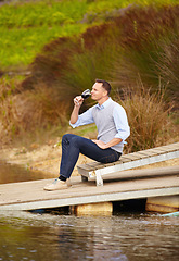 Image showing Thinking, river and a man drinking wine outdoor in nature on his farm for agriculture or sustainability. Water, glass and idea with a male person sitting on the pier to drink alcohol alone outside