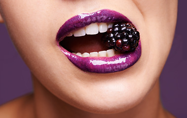 Image showing Woman lips, purple lipstick with blackberry and makeup, shine and creativity with beauty isolated on studio background. Closeup of fruit between female model teeth, cosmetic product and cosmetology