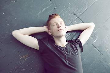 Image showing Relax, overhead and a man lying on the floor, hands behind head to sleep, rest or dream of peace. Quiet, sleeping and lifestyle with a young ginger male person relaxing on the ground from above