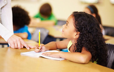 Image showing School, education and kids with a student girl in a classroom, writing while talking to her teacher. Children, learning and study with an adorable female kid at a desk in class for child development