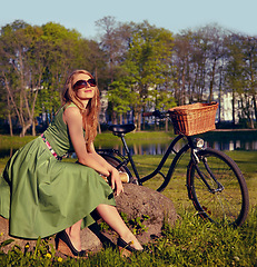 Image showing Happy, smile and bicycle with woman in park for cycling, freedom and nature. Spring, relax and peace with female person and bike resting on rock in grass field for health, summer break and happiness