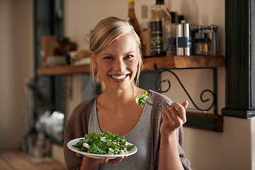 Image showing Young, woman and eating a salad in kitchen with a smile with wellness and lettuce for cooking. Girl, healthy and vegetables on plate for nutrition or diet in house with hungry person in the usa.