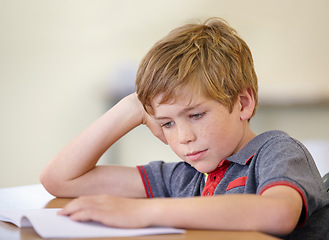 Image showing School, education and a boy reading a book at his desk in a classroom for studying or child development. Kids, learning and bored with a young male student child in class to study for an exam or test