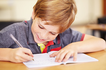 Image showing School, education and a student boy writing in a book while sitting at his desk in a class room for learning. Kids, study and notebook with a young male pupil in a classroom for child development