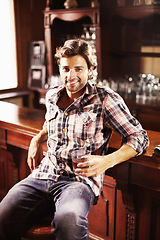 Image showing Portrait, smile and man with whiskey in pub sitting by counter alone. Alcohol, happiness and male person in bar for drinking liquor, beverage or drink in tavern, relaxing and enjoying time alone.