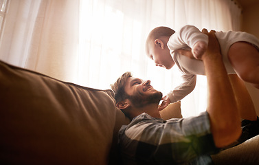 Image showing Funny, dad and lifting baby on sofa in home living room, playing or bonding together. Happy, care and father holding infant, newborn or child on couch in lounge, having fun and enjoying quality time.