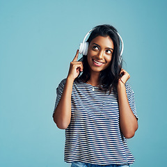 Image showing Woman, thinking and headphones with music in studio with happiness and web audio. Blue background, Indian female person and young model listening, hearing and streaming a song with smile and mockup