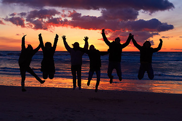 Image showing Beach, sunset and silhouette of jumping friends in nature, freedom and celebrating travel outdoor. Shadow, jump and group of people at the ocean and sunrise for adventure, celebration or sea vacation